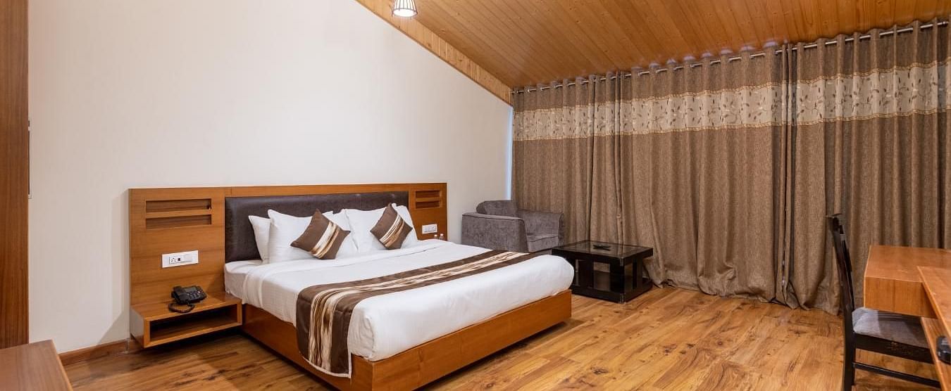 This photo captures a cosy and inviting hotel room with a warm wood-panelled ceiling and large windows that bring in plenty of natural light  | DLS Serenity Resort and Spa